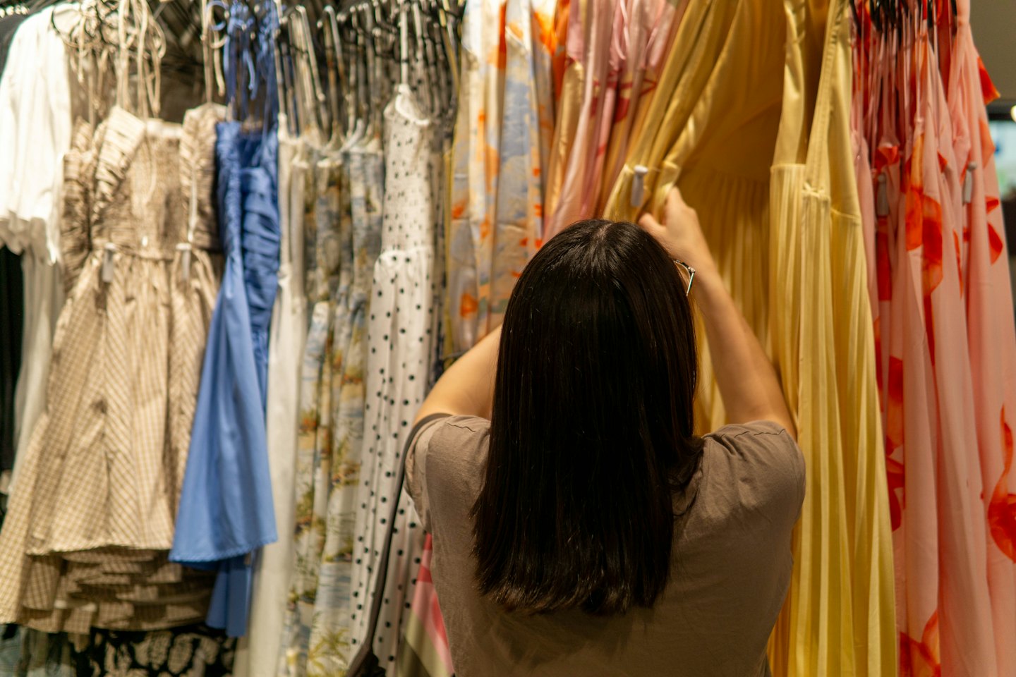 Woman shops for yellow dresses in a clothing store.